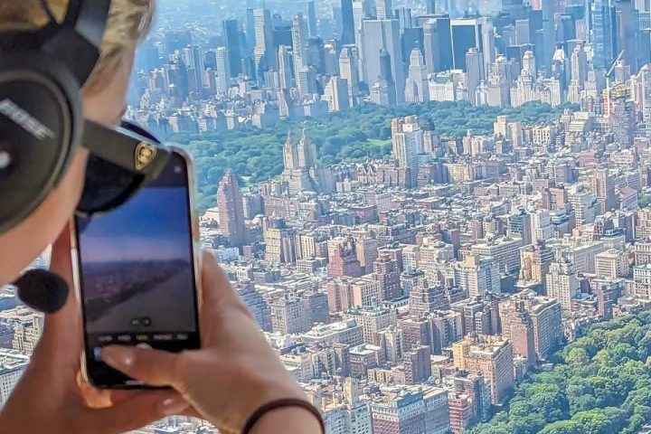 Person in helicopter taking photo of New York City skyline with smartphone.