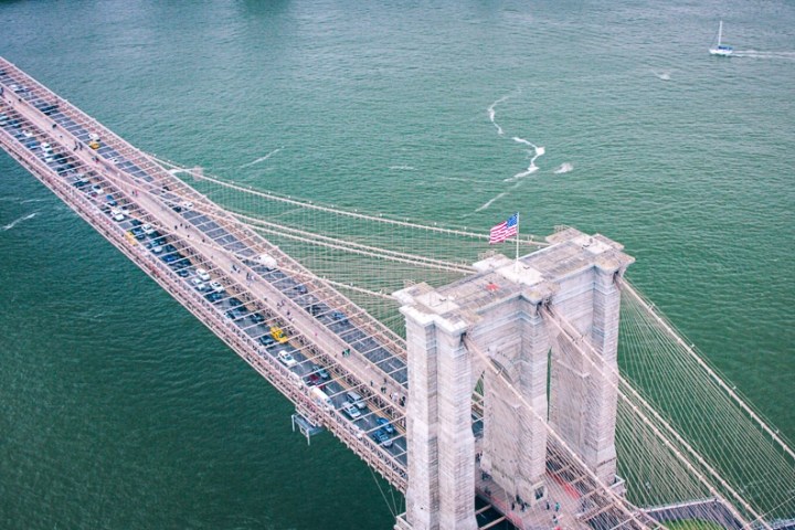 Aerial view of a busy suspension bridge over a river with a boat visible in the water.