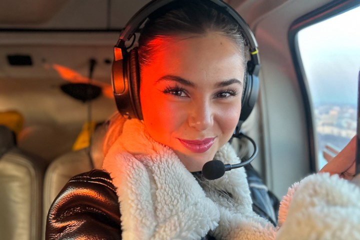 Person in a helicopter wearing a headset and black leather jacket with white fur collar.