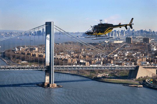 helicopter flying over water with bridge and NYC in background