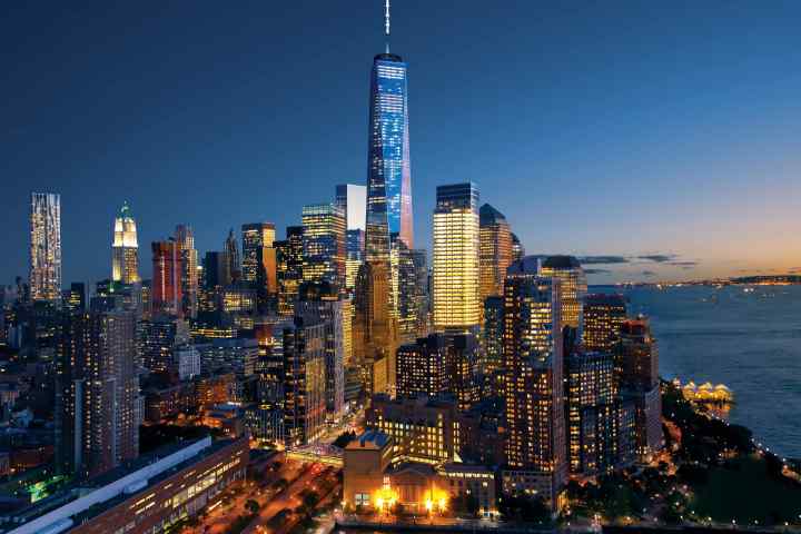 Aerial view of illuminated New York city skyline by water at dusk.