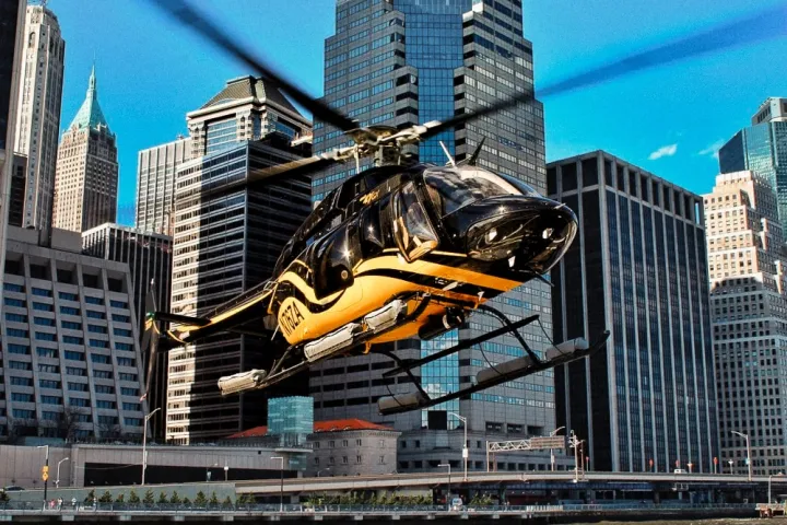 Black and yellow helicopter hovering near skyscrapers in a NYC cityscape.