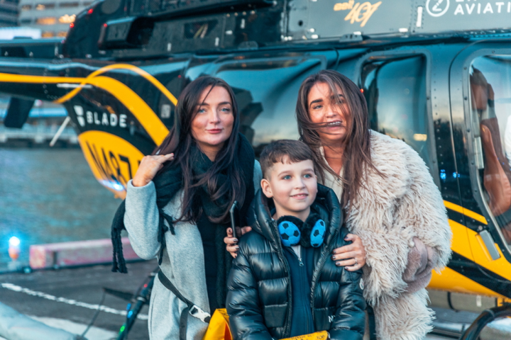 Two women and a child in front of a helicopter on a helipad in NYC.