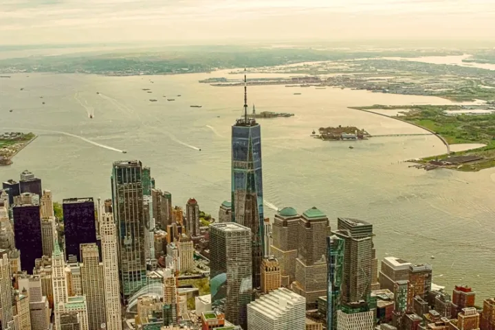 Aerial view of a New York City skyline next to a river with distant greenery.